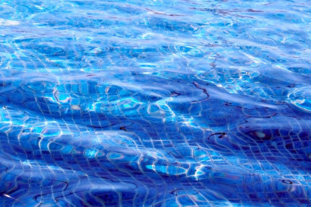Clear blue water in a saltwater swimming pool with sunlight reflections, perfect for summer and relaxation themes.