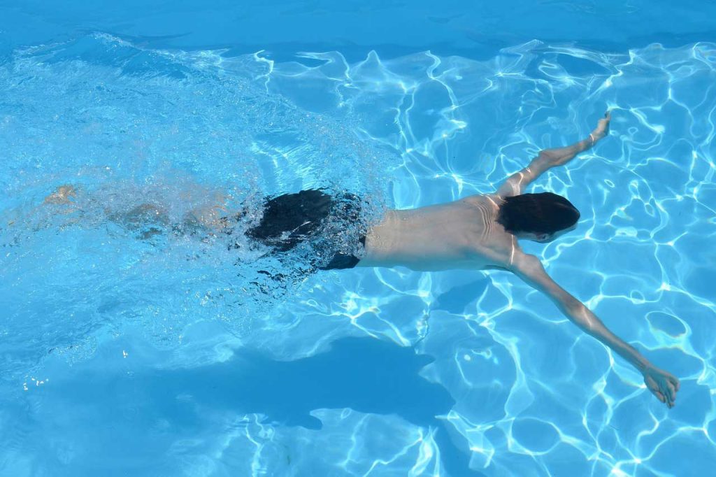Person swimming in a clear blue saltwater swimming pool, viewed from above, creating ripples in the water.