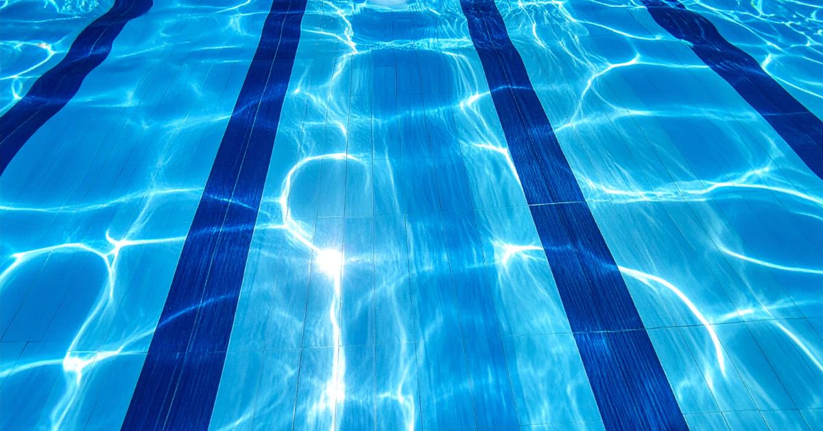 Modern swimming pool interior with blue tile finish and clear water reflecting sunlight.