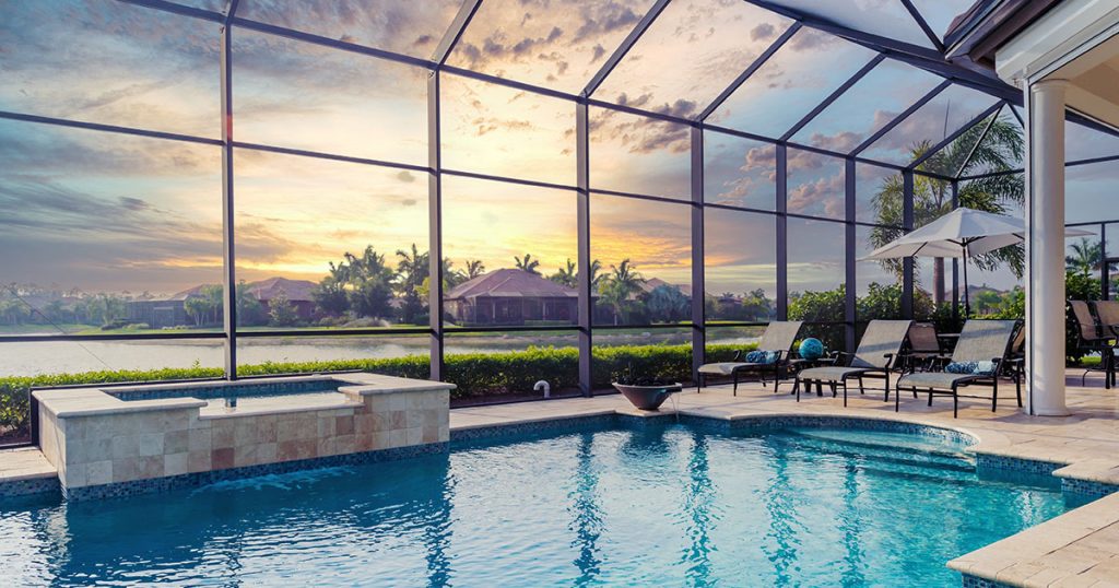 A screened-in pool with clear cerulean water and Florida homes on the horizon.
